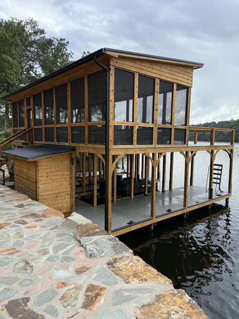 Interior view of a screened-in wooden porch with a vaulted ceiling, ceiling fan, and black metal balusters overlooking a backyard.