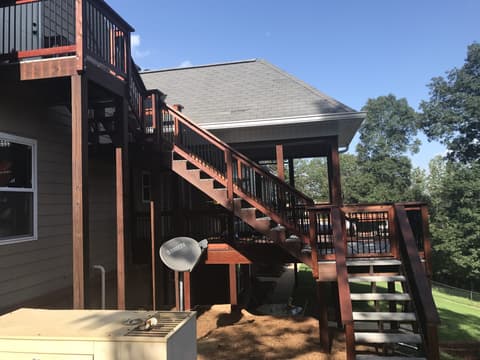 A screened-in porch with dark stained wood ceilings, skylights, and wicker furniture overlooking a wooded backyard.