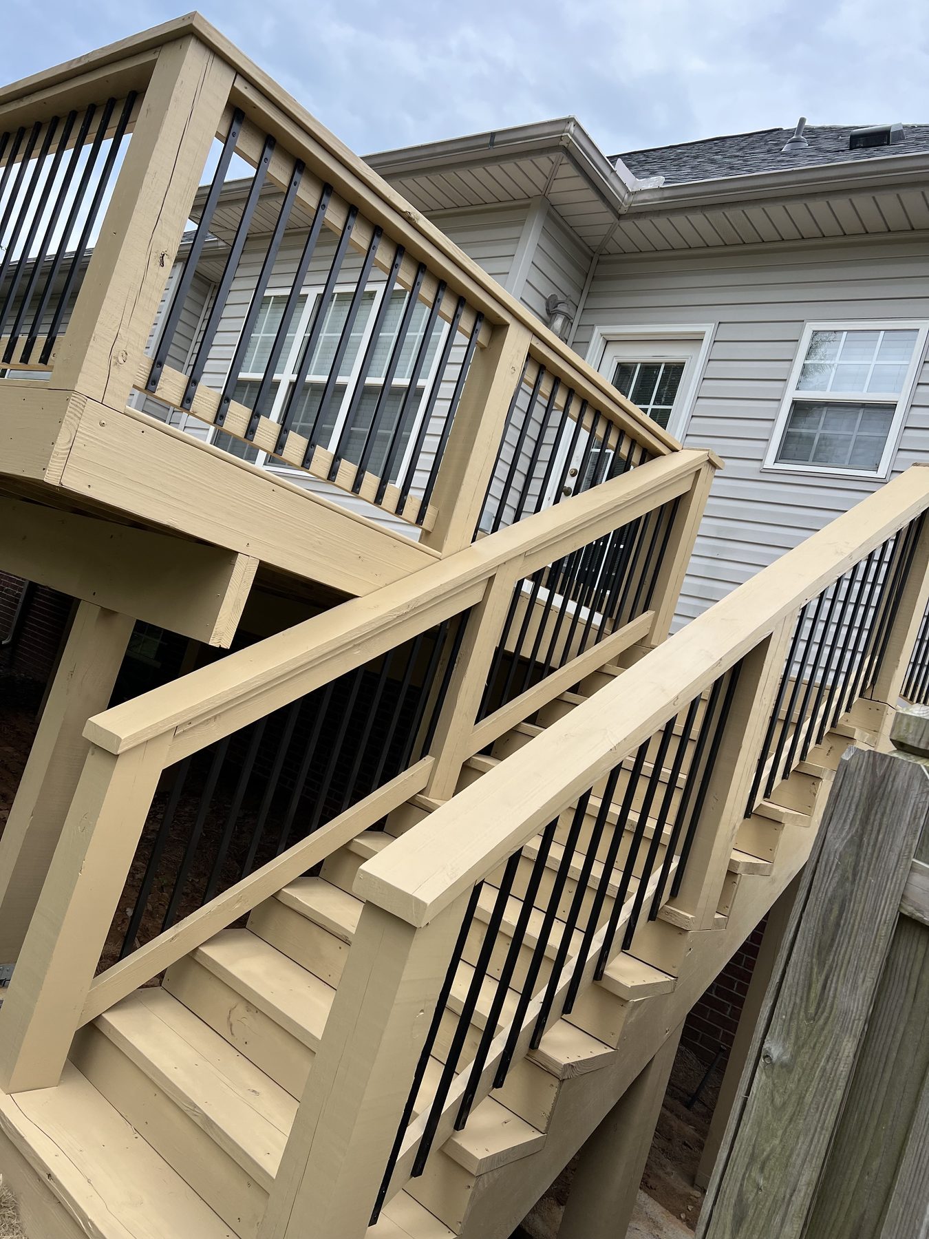 Interior view of a screened-in wooden porch with a vaulted ceiling, ceiling fan, and black metal balusters overlooking a backyard.