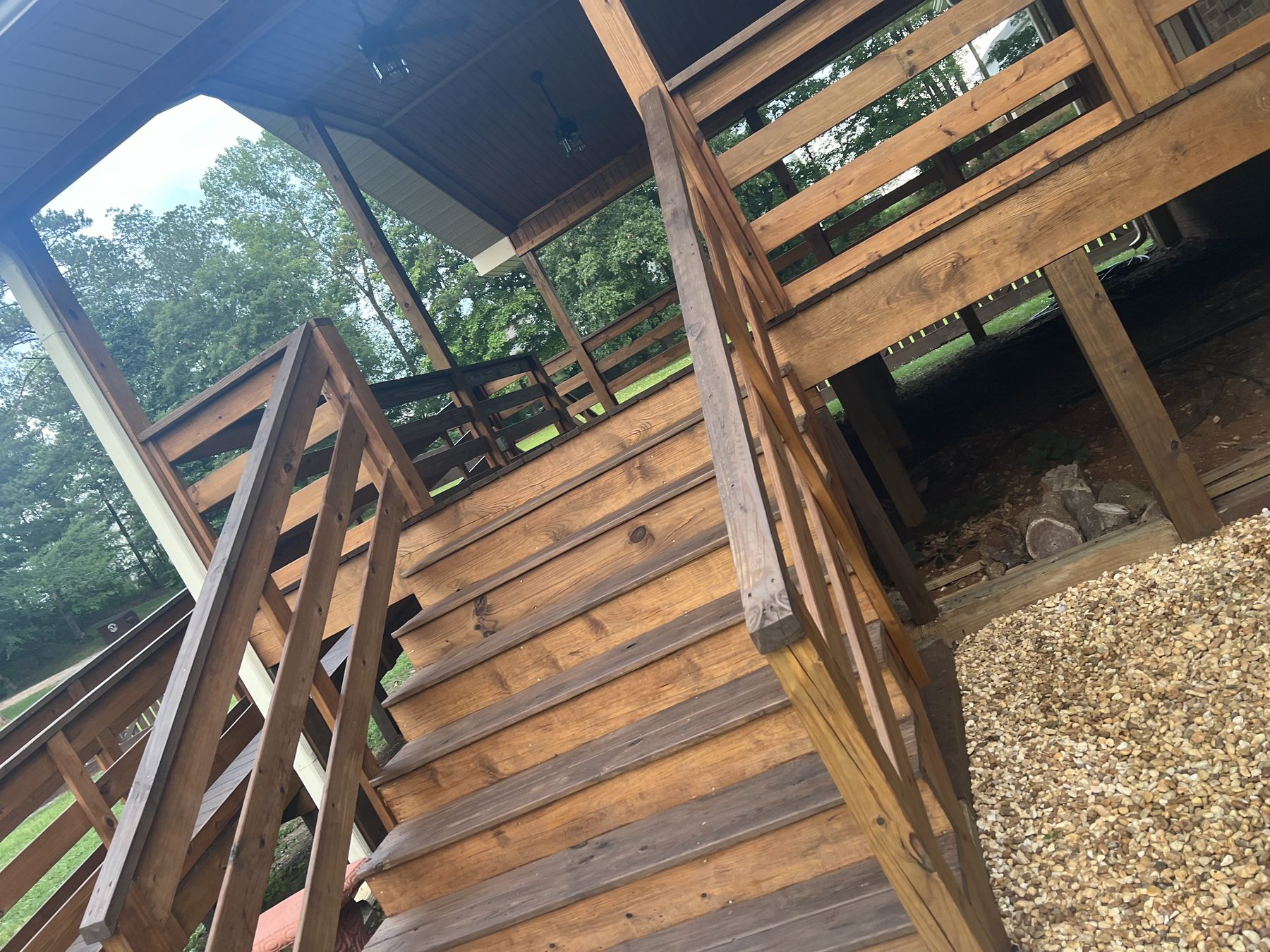 Interior view of a screened-in wooden porch with a vaulted ceiling, ceiling fan, and black metal balusters overlooking a backyard.