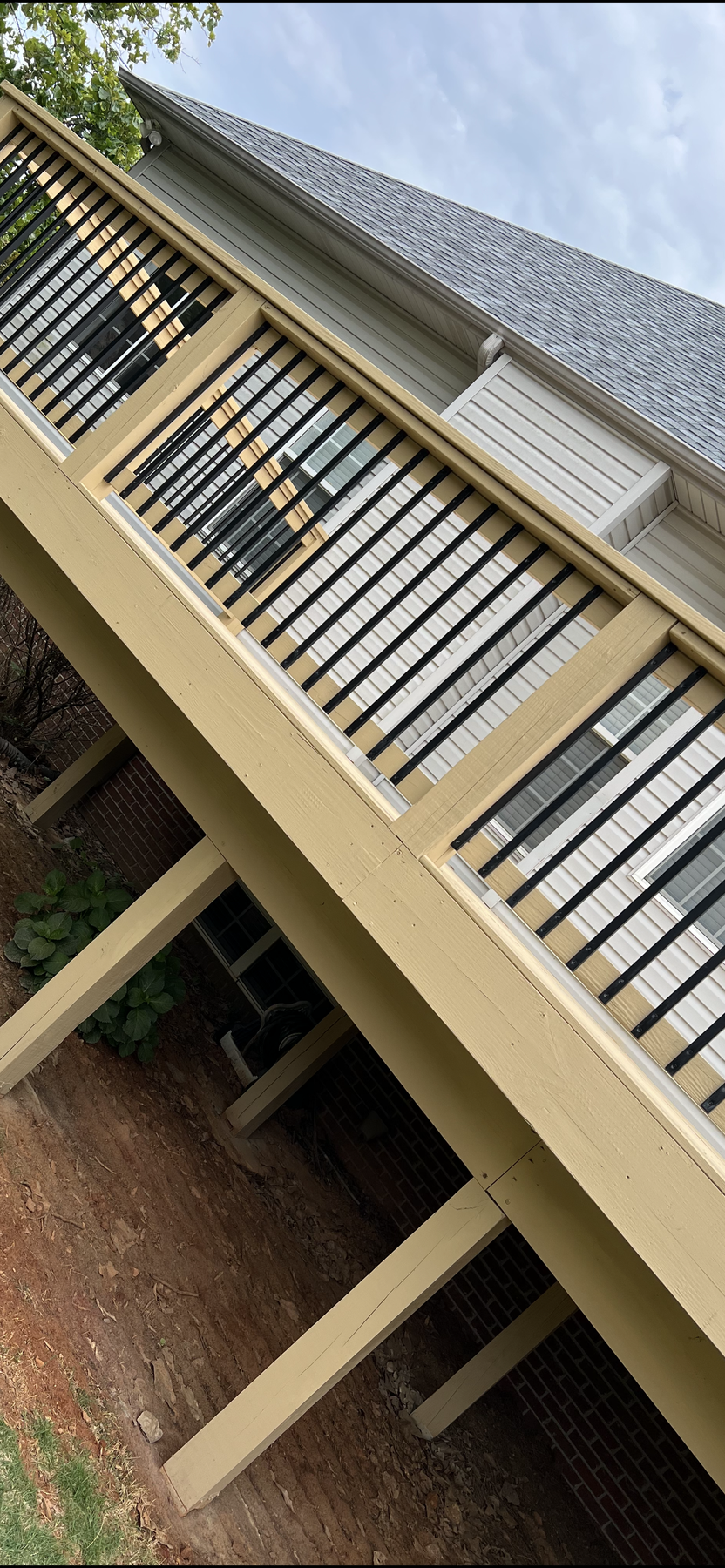 Interior view of a screened-in wooden porch with a vaulted ceiling, ceiling fan, and black metal balusters overlooking a backyard.
