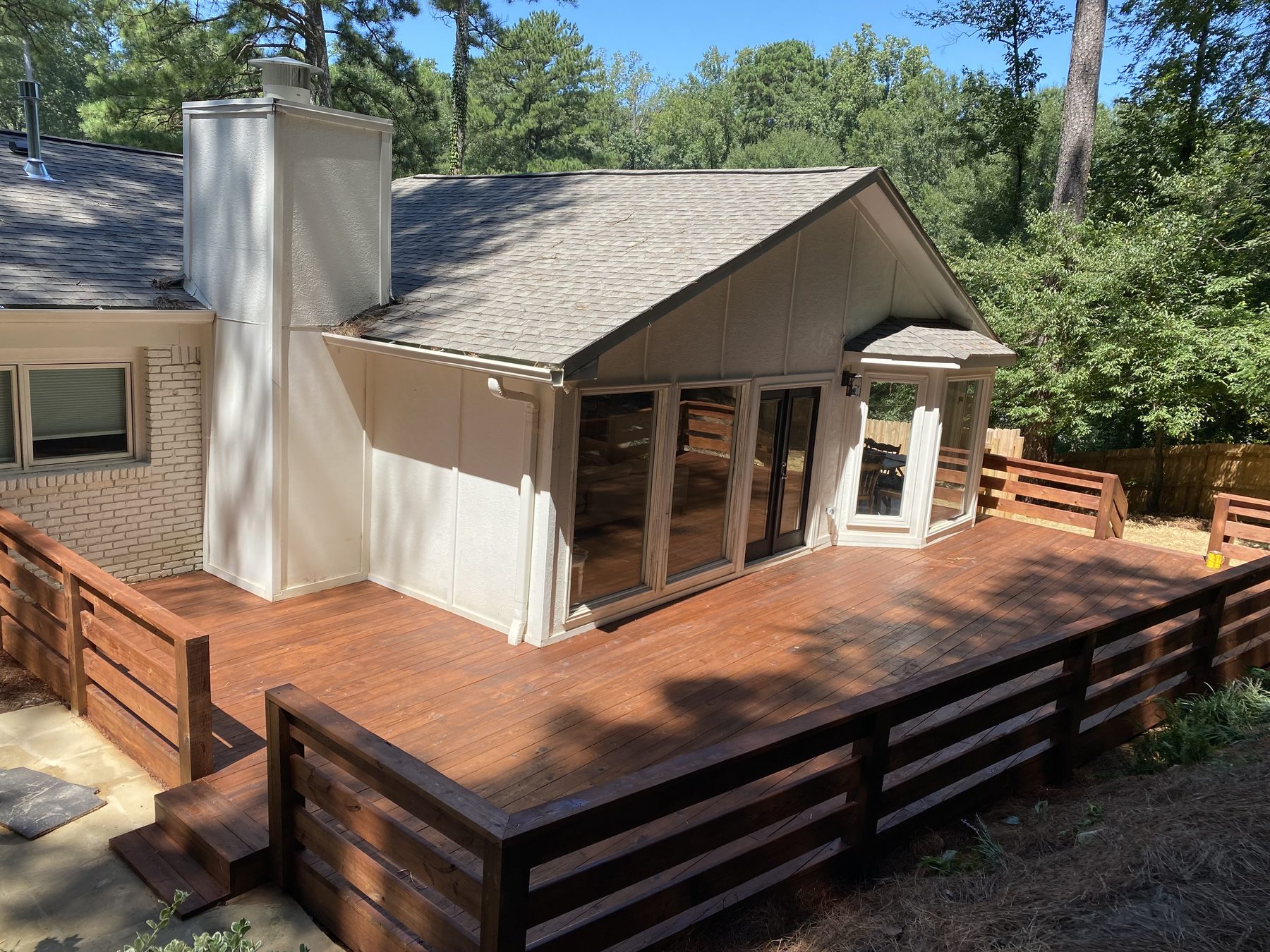 A professionally stained dark wood deck with white railings and a grill in the background.